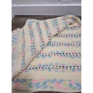 May include: A handmade crochet blanket featuring a cream-colored base with alternating horizontal stripes of solid cream yarn and openwork sections interspersed with variegated pastel yarn in shades of light pink, baby blue, and soft yellow.