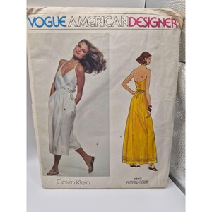 以下が含まれることがあります： Calvin KleinのVogue American Designer型紙封筒、番号1665。表面には、白いラップドレスと黄色いストラップレスのマキシドレスのイラスト、テキスト、および白いドレスの写真が掲載されています。