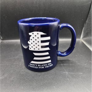 Może przedstawiać: Granatowy ceramiczny kubek z białym graficznym profilem z gwiazdami i paskami oraz napisem "DON'T BLAME ME, I VOTED FOR TRUMP." Kubek ma zakrzywiony uchwyt.