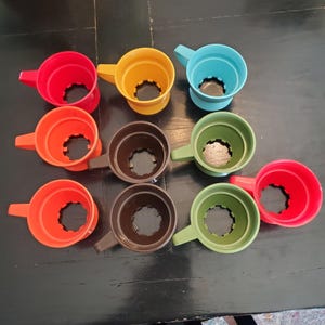 May include: Set of ten colorful plastic coffee mugs with handles. The mugs are in various colors, including red, orange, yellow, green, blue, and brown.