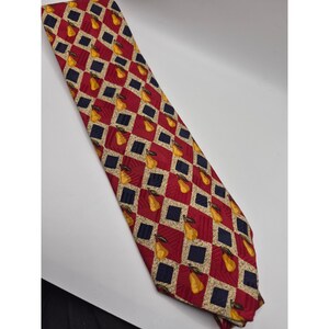 Peut inclure: Une cravate présentant un motif répétitif de losanges rouges, bleu marine et beiges. Chaque losange rouge contient une petite illustration de poire jaune avec une tige verte. Le tissu présente une texture subtilement côtelée en diagonale.