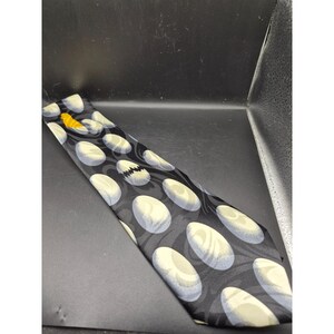 May include: A black necktie with a repeating pattern of white and gray ovals. A yellow bird is near the top of the tie. The tie has a whimsical design.