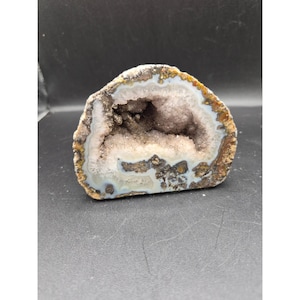 May include: A geode cut open to reveal a sparkling interior. The outer shell is a mix of brown, tan, and white, with a crystalline center in shades of lavender and gray. The geode is a natural, decorative item.