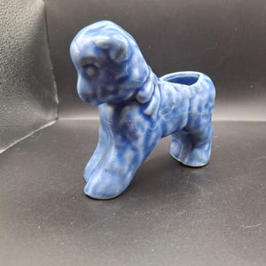 Könnte beinhalten: Ein blauer Keramik-Lamm-Pflanztopf mit strukturierter, craquelierter Glasur. Das Lamm steht mit einer kleinen Öffnung auf dem Rücken zum Bepflanzen. Das Lamm ist hellblau mit weißen Akzenten.