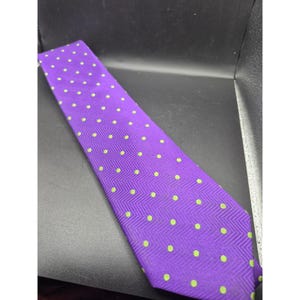 May include: A purple necktie with a repeating pattern of small, light green polka dots. The tie has a subtle chevron weave texture. This formal accessory is suitable for business or special occasions.