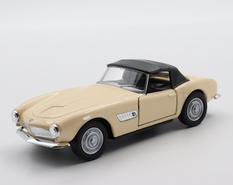 May include: A beige toy car model of a classic convertible with a black top. The car has a detailed interior and exterior, including chrome accents and a BMW logo on the front.