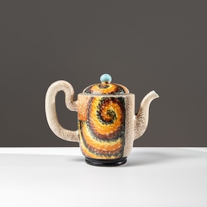 May include: A ceramic teapot with a swirling pattern in shades of brown, yellow, and black. The teapot has a light blue knob on the lid and a spout on the side.