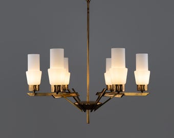 May include: A vintage brass chandelier with six frosted glass shades. The light fixture has a central stem and radiating arms, creating a starburst design. The shades are cylindrical with a wider base and top.