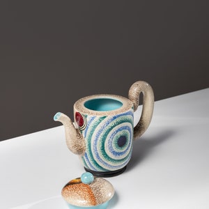 May include: A ceramic teapot with a blue, green, and brown geometric pattern. The teapot has a lid with a similar pattern.