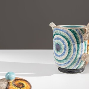 May include: A blue and green ceramic teapot with a swirling pattern and a matching lid. The teapot has a unique, abstract design.