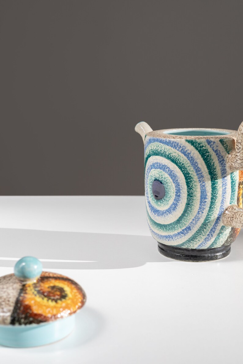 May include: A blue and green ceramic teapot with a swirling pattern and a matching lid. The teapot has a unique, abstract design.