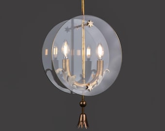 May include: A gold-toned chandelier with a clear, circular shade. The chandelier features three light bulbs, decorative star accents, and a floral-inspired base. The fixture hangs from a gold rod and has a decorative bottom element.