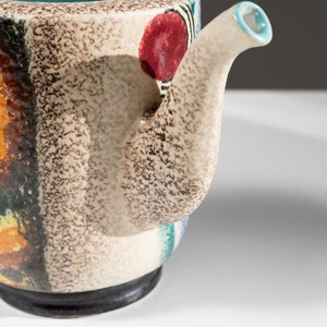 May include: A ceramic teapot with a speckled brown glaze and colorful abstract designs. The teapot has a spout and a handle.