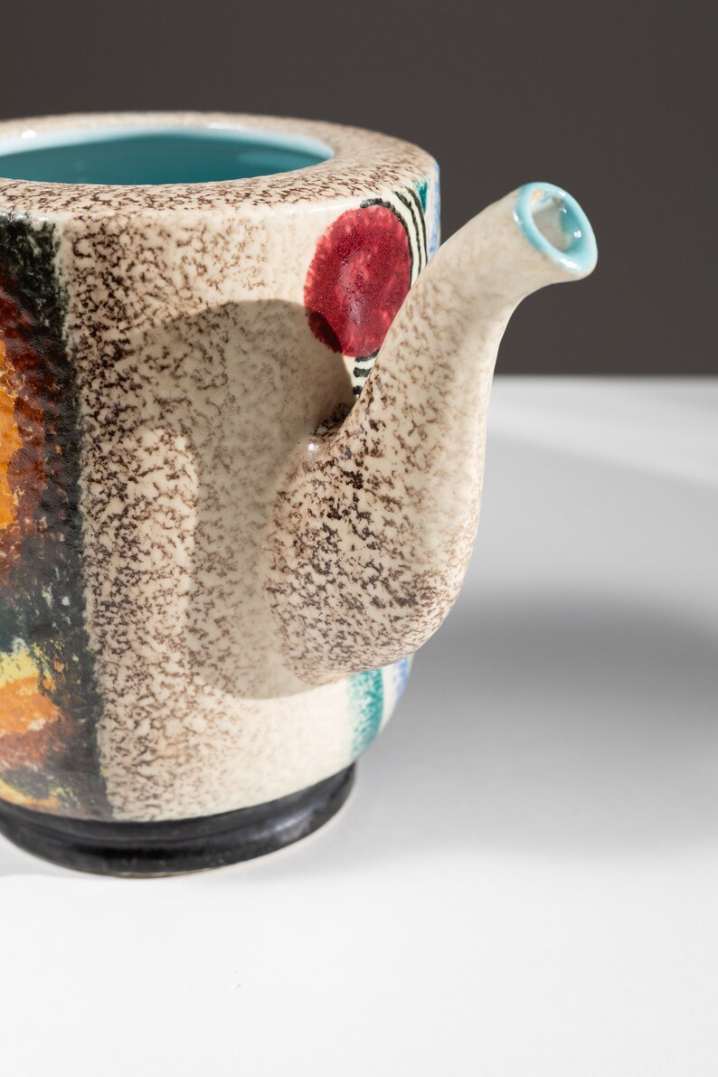 May include: A ceramic teapot with a speckled brown glaze and colorful abstract designs. The teapot has a spout and a handle.