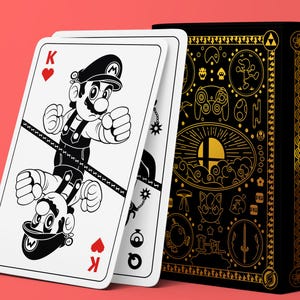 Puede incluir: Una baraja de cartas con una ilustración en blanco y negro de Mario en la carta del Rey de Corazones. La baraja es negra con detalles dorados e iconos de personajes. El fondo es de color coral sólido.