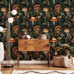 May include: A dark green wallpaper with a repeating pattern of orange jellyfish, mushrooms, and fish. A wooden cabinet, floor lamp, and potted plants are in front of the wallpaper. The room is decorated in a natural, botanical theme.