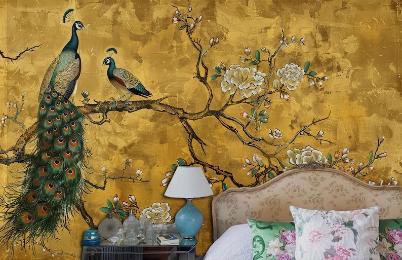 K&ouml;nnte beinhalten: Eine goldfarbene Wandmalerei mit einem gro&szlig;en Pfau und einem kleineren Pfau, der auf einem Ast mit wei&szlig;en Bl&uuml;ten sitzt. Die Wandmalerei befindet sich in einem Schlafzimmer mit einem Bett und einer Lampe.