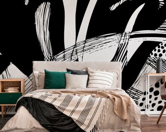 May include: A bedroom with a black and white abstract art print on the wall. The bed has a beige duvet with a black and white striped throw blanket. There are green and gray throw pillows on the bed. A wooden nightstand with a green drawer is next to the bed.