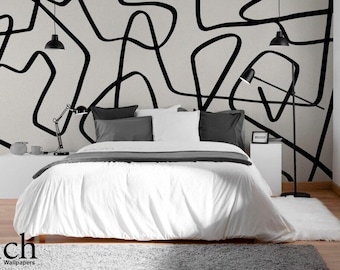 May include: A modern bedroom with a white bed, gray pillows, and a gray blanket. The wall features a black and white abstract design. Black lamps and a small rug complete the room's decor.