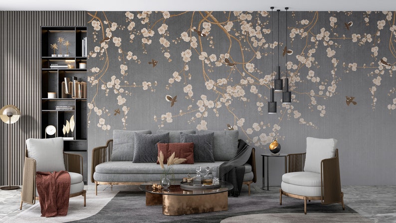 May include: A living room interior design with a gray sofa and two armchairs. The wall features a gray wallpaper with a floral pattern of white blossoms and brown branches. The wallpaper has a subtle textured look.