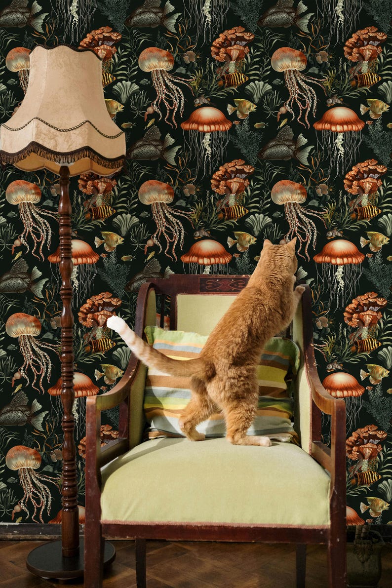 May include: An orange tabby cat stands on its hind legs, reaching towards a vintage armchair. The background features a dark wallpaper with a repeating pattern of jellyfish, fish, and mushroom-like shapes. A floor lamp with a beige shade is on the left.