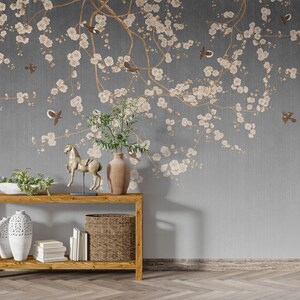 May include: A wooden console table with two shelves, a white ceramic vase, a wicker basket, and a gold horse figurine. The table is in front of a gray wall with a floral wallpaper design featuring white blossoms and brown birds.