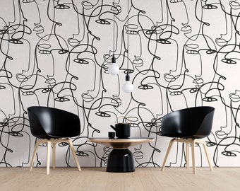 May include: Two black chairs with wooden legs and a black round table with a gold rim and a black teapot on top, all in front of a white wall with a black and white line drawing pattern of abstract faces.