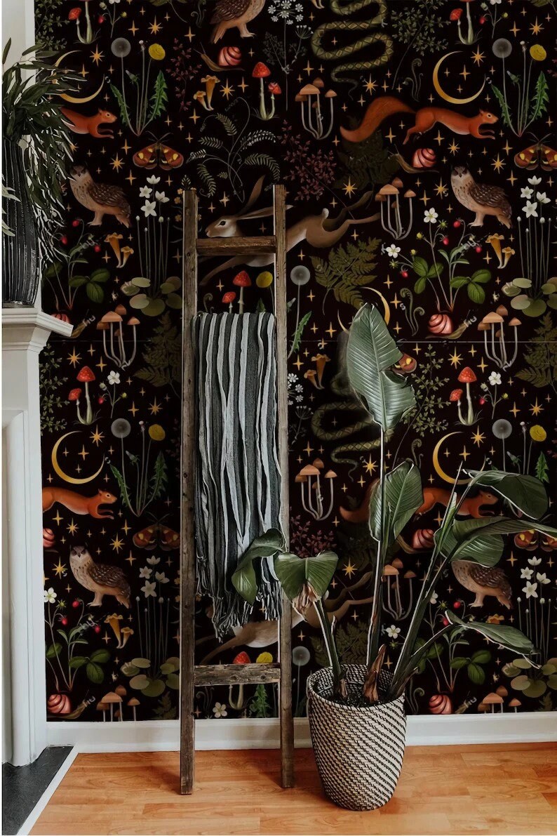 May include: A black and white wallpaper with a repeating pattern of woodland creatures, mushrooms, and stars. The wallpaper is displayed on a wall with a wooden ladder and a potted plant in front of it.