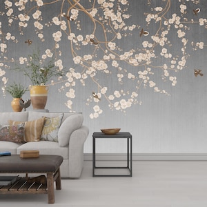 May include: A white couch with pillows sits in front of a wall with a gray and white floral wallpaper featuring a branch of cherry blossoms with small brown birds. A small black side table sits next to the couch.