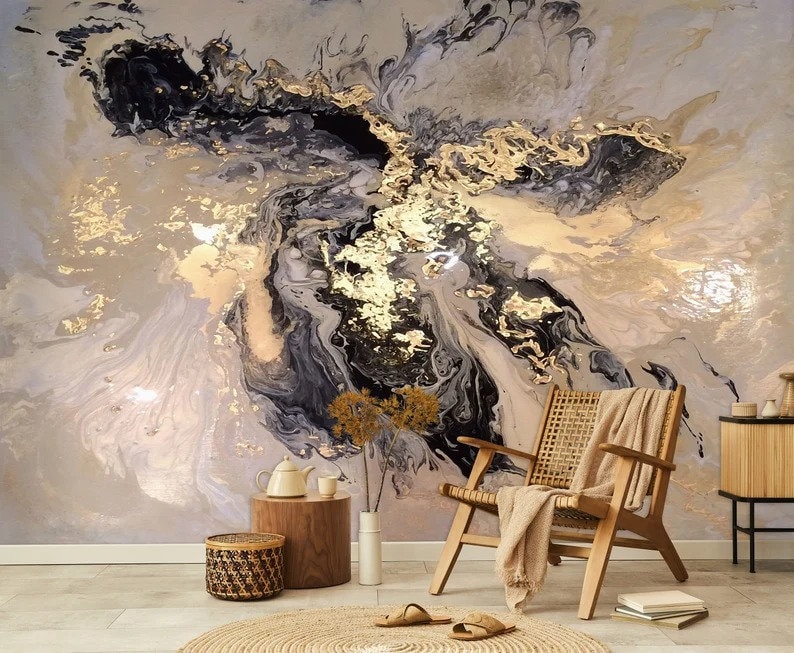May include: Abstract wall art featuring a swirling pattern of black, gold, and white paint. The art is displayed in a living room setting with a chair, a side table, and a vase of flowers.