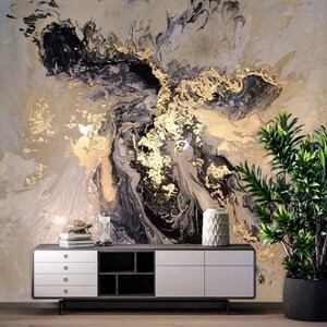 May include: Abstract wall art featuring a swirling pattern of black, gold, and white paint. The art is displayed on a wall with a white cabinet and a potted plant in the foreground.