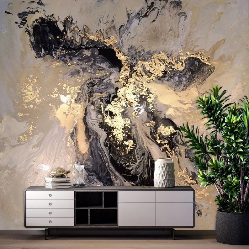 May include: Abstract wall art featuring a swirling pattern of black, gold, and white paint. The art is displayed on a wall with a white cabinet and a potted plant in the foreground.