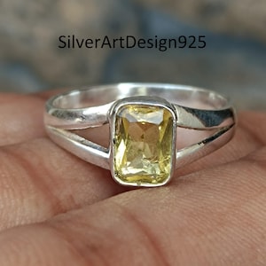 Op de afbeelding: Een zilveren ring met een rechthoekige, gele edelsteen. De ring heeft een gespleten bandontwerp, met de edelsteen in een bezel-zetting. De tekst "SilverArtDesign925" is zichtbaar.