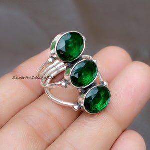 May include: A silver ring featuring three oval, emerald-green gemstones. The ring has a unique design with the gemstones set in individual bezels and connected by delicate silver bands. The text "SilverArtDesign925" is visible.