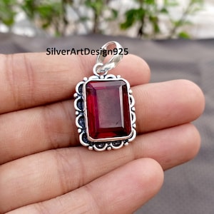 May include: A rectangular pendant with a deep red gemstone set in a decorative silver frame. The frame has a scalloped edge and a loop for a chain. The text "SilverArtDesign925" is visible.
