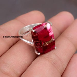 Könnte beinhalten: Ein Silberring mit einem rechteckigen, tiefroten Edelstein mit weißen und goldenen Adern. Der Ring hat ein poliertes Silberband, und der Edelstein wird von vier Krappen gehalten. Der Text "SilverArtDesign925" ist sichtbar.