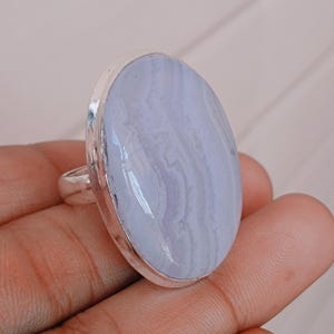 Puede incluir: Un anillo de plata con una gran piedra ovalada de ágata azul. El ágata tiene un patrón de remolino de azul claro y oscuro.