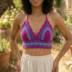 Puede incluir: Top halter de ganchillo hecho a mano en tonos fucsia, azul y lavanda. El top presenta un borde festoneado y un diseño de cuello halter. El patrón de ganchillo crea un aspecto texturizado y llamativo. El top se usa con un pantalón de color claro.