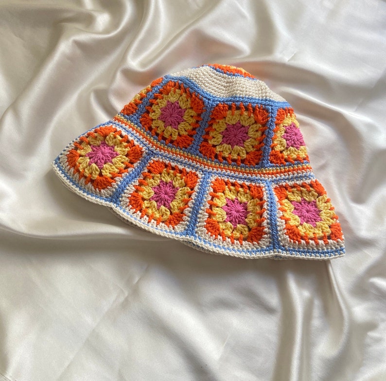 May include: A crocheted bucket hat with a white base and colorful granny squares in shades of orange, yellow, pink, and blue.