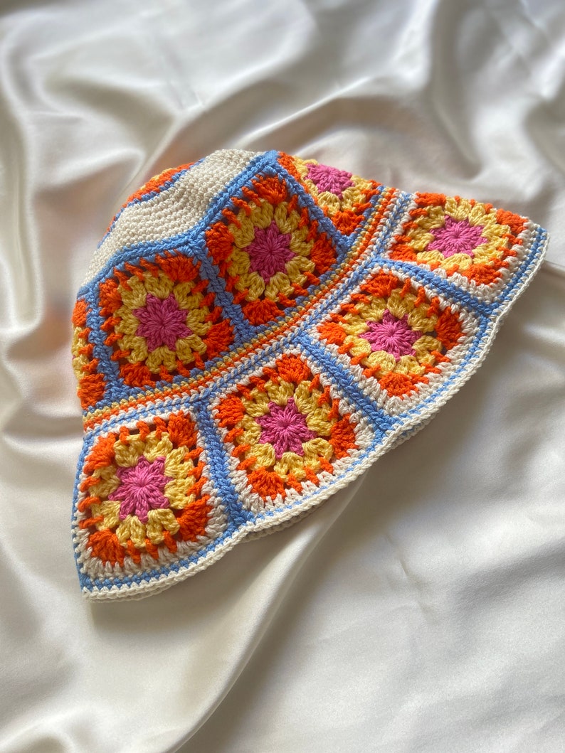 May include: A crocheted bucket hat with a white base and colorful granny squares in shades of orange, yellow, pink, and blue.