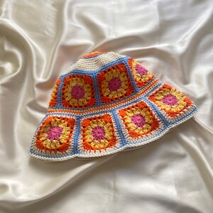 May include: A crocheted bucket hat with a white base and colorful squares in shades of orange, yellow, and pink.
