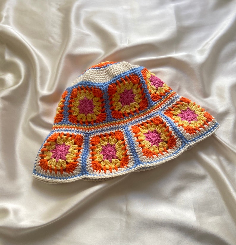 May include: A crocheted bucket hat with a white base and colorful squares in shades of orange, yellow, and pink.