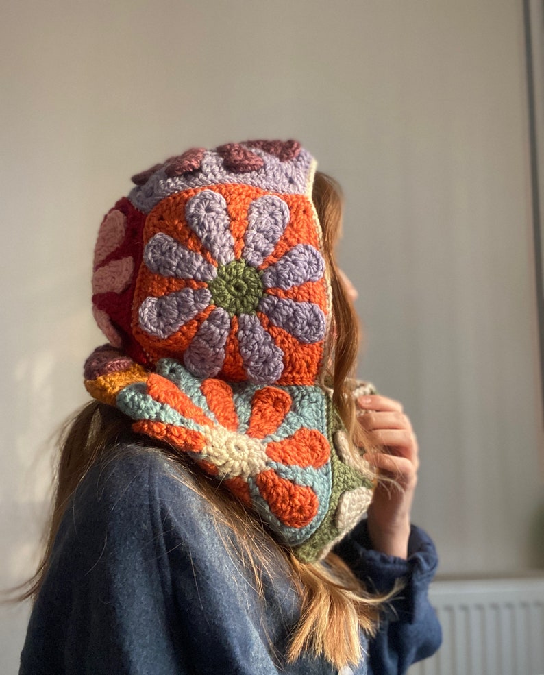 May include: A colorful crocheted hooded cowl with a floral pattern in shades of orange, purple, green, and pink.
