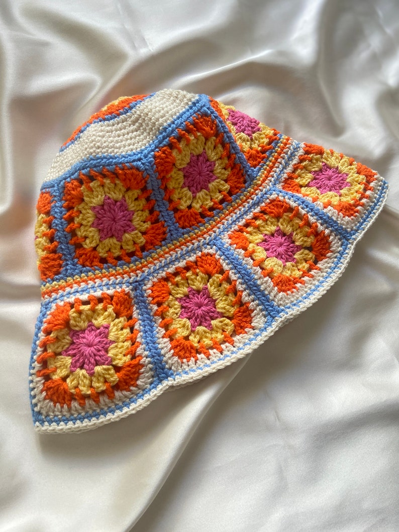 May include: A crocheted bucket hat with a white base and colorful squares in shades of orange, yellow, pink, and blue.