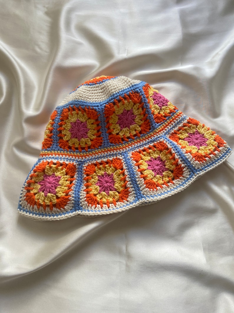 May include: A crocheted bucket hat with a white base and colorful granny square pattern in shades of orange, yellow, pink, and blue.