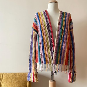Puede incluir: Un cárdigan de crochet a rayas de colores con detalles de flecos en el dobladillo y las mangas.
