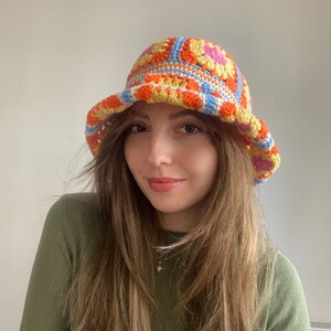 May include: A crocheted bucket hat with a colorful geometric pattern in shades of orange, yellow, pink, and blue.