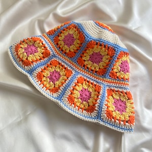 May include: A crocheted bucket hat with a white base and colorful granny squares in shades of orange, yellow, pink, and blue.