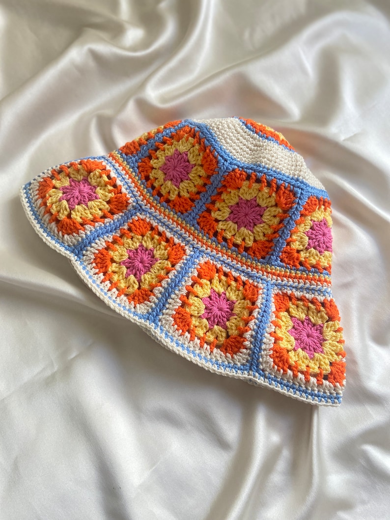 May include: A crocheted bucket hat with a white base and colorful granny squares in shades of orange, yellow, pink, and blue.