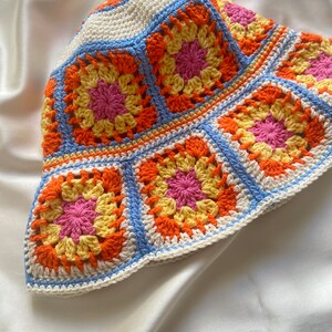 May include: A crocheted bucket hat with a colorful granny square pattern in shades of orange, yellow, pink, and blue.